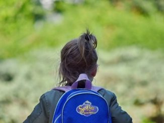 Un.e enfant de dos avec un cartable.